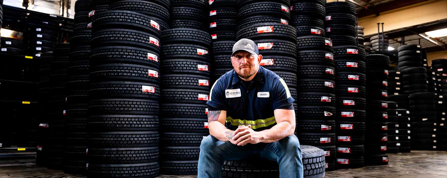 East Bay Tire employee sitting on a tire in front of stacks of tires